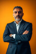 © wolfhound911 - A confident middle-aged Arabian man in a tailored suit, arms crossed against a vibrant orange background, projecting authority and determination.