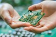 © vilaiporn - A close-up of hands holding a green circuit board with intricate designs, showcasing technology and innovation in electronics.