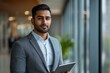 © Divyesh - Confident Indian business man leader looking aside walking in office. Busy professional businessman going in hallway holding digital tablet thinking of work plan using tab computer. Generative AI