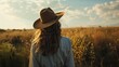 © VK Studio - A woman in a wide-brimmed hat stands in a golden field at sunset, absorbed in the beauty and tranquility of nature around her.