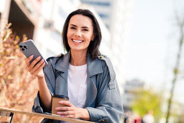 Sticker - Photo of shiny attractive lady dressed grey coat smiling sitting cafe drinking tea communcating modern device outdoors town street