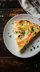 Potato and carrot pie slice garnished with parsley, presented on a white plate atop a dark wooden table