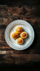 Four sweet buns with a yellow topping and white sprinkles are sitting on a white plate on a rustic wooden table