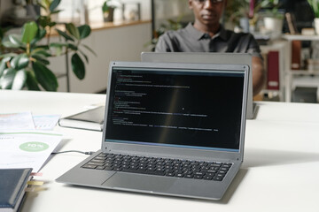 Wall Mural - Medium close up of silver laptop with codes on black screen in modern office