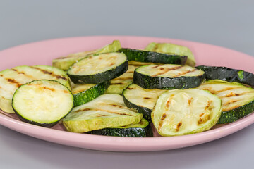 Grilled circles of zucchini and vegetable marrows on pink dish