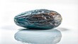 © Wahyu_T - A single, dried, blue date fruit with a wrinkled texture and a brown spot, resting on a white surface and reflecting in the light.