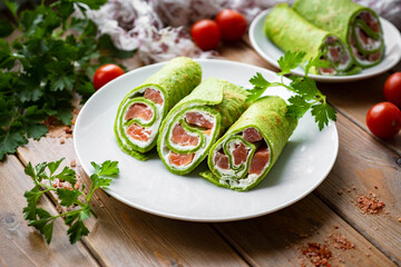 Spinach pancakes on a white plate on a wooden table. Green pancakes with fish filling for breakfast. Close-up.