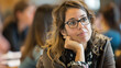 © Preeyada - Thoughtful Woman with Glasses Listening Attentively in a Classroom Setting