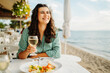 © Dusan - Young caucasian woman eating greek salad and drinking wine by the sea