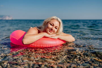 Wall Mural - A woman is laying on a red inflatable ring in the ocean