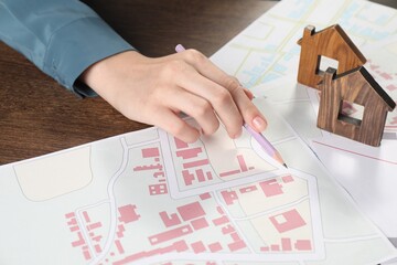 Wall Mural - House hunting. Woman with maps and house figures at wooden table, closeup