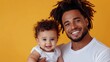 © Pinklife - An affectionate father holds his cheerful baby with a radiant yellow background, showcasing a moment filled with happiness, warmth, and familial love.