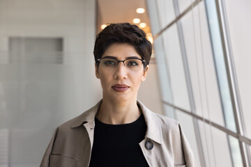 Serious confident short haired businesswoman in stylish glasses and casual clothes posing for portrait in in office alone, looking at camera. Business leader, entrepreneur woman head shot