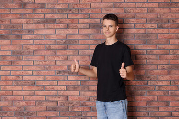 Wall Mural - Teenage boy wearing black t-shirt and showing thumbs up near brick wall