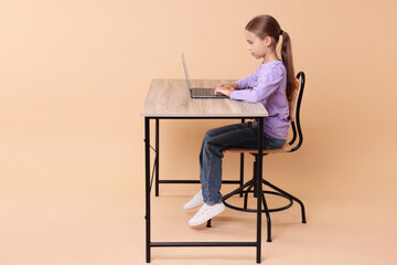 Wall Mural - Girl with correct posture using laptop at wooden desk on beige background