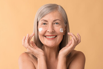 Poster - Senior woman with face cream on beige background