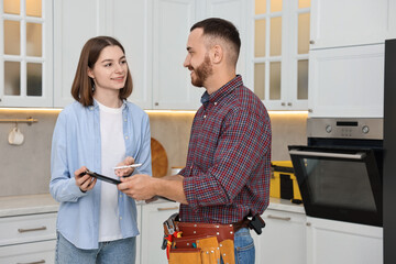 Poster - Smiling woman and repairman signing documents near oven in kitchen