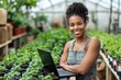 © Pooja - Pretty young African American female farmer or woner oh large hothouse with laptop standing against long tables with seedlings, Generative AI