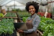 © Pooja - Pretty young African American female farmer or woner oh large hothouse with laptop standing against long tables with seedlings, Generative AI