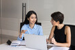 © fizkes - Two positive diverse female business colleagues talking at laptop, using modern technology for teamwork, discussing online startup project, cooperation strategy, sitting at meeting table