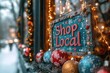 © zulie - A wooden sign with the words 'Shop Local' displayed in a storefront window decorated with Christmas ornaments and lights.