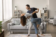 © fizkes - Happy active married couple dancing in stylish living room interior, enjoying activity at home together. Positive strong husband embracing wife in romantic social dance with passion