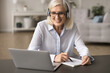 © fizkes - Aged woman wear headphones engaged in online study using laptop, participating in video call or virtual meeting, taking notes. Teacher lead on-line lesson, explain topic to learner. Tuition, education