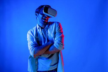Poster - Handsome smart man dancing and moving gesture to music by using VR glasses with neon light background. Caucasian male gamer standing while moving to pop music wearing technology innovation. Deviation.