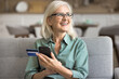 © fizkes - Happy mature woman holds debit card and cellphone, paying for streaming services and subscriptions, booking flights, hotels, rentals, reserving tickets. Client of on-line shopping, money transfer apps