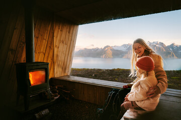Wall Mural - family mother and daughter talking in cozy mountain hut cabin with fireplace and panoramic window mo