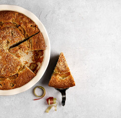 A piece of delicious rhubarb pie lays nearby baked dish with pie . top view , copy space