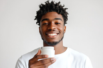 a young adult african american man, smiling charmingly as he holds a small jar of cream. the white b