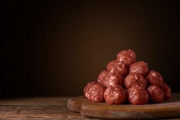 raw minced meatballs lie in a conical pile on a wooden cutting board on a plank table on a dark brown soft background with light gradient. artistic moody photo in a rustic style with copy space