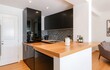 © TheseusStock - Modern kitchen interior with bar counter, black cabinets and wooden countertop.  A coffee machine stands on one side of it.