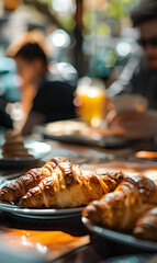 Wall Mural - Fresh croissants on breakfast table in warm morning sunlight, people gathered in the background, creating cozy, inviting atmosphere for brunch or coffee or tea