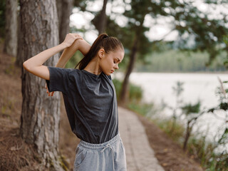 young woman stretching outdoors by the lakeside, wearing a casual grey t shirt and sweatpants, enjoy