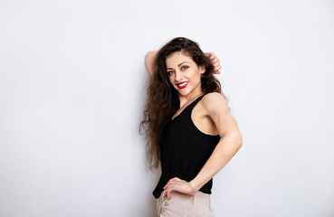 Wall Mural - Happy relaxing toothy smiling make-up woman with red lipstick, long brown hair standing in black top near the wall on empty copy space studio blue background. Portrait