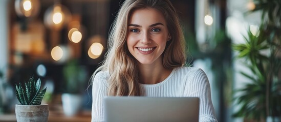 Wall Mural - A young woman smiles brightly as she sits in a cafe, working on her laptop computer.