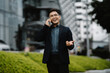© Nittaya - Joyful Business Call:  A smiling Asian businessman in a suit makes a phone call outdoors, expressing excitement and success. His positive energy is infectious.