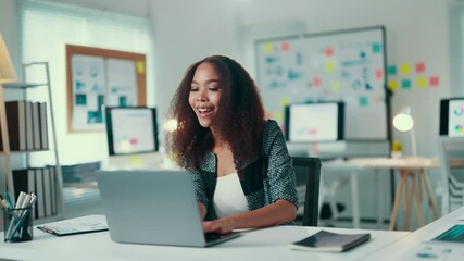 Aufkleber - African american woman with curly hair is sitting at her desk in a bright startup office, typing on her laptop and smiling