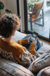 © Degimages - Person sitting on a couch, intently adjusting home security cameras through smartphone app interface