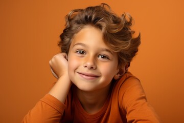 Portrait of a cute little boy with long curly hair, isolated over orange background.