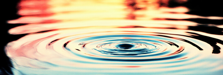 Poster - Water drop ripples on a still surface with a soft, colorful background.