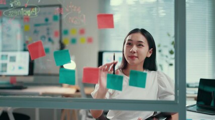 Poster - Young asian businesswoman organizes thoughts by writing on sticky notes while standing in an office, showcasing a creative approach to planning and project management