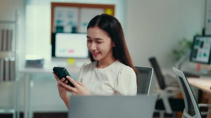 Aufkleber - Young professional woman smiling while using a smartphone at her desk. Bright and clean workspace enhances her cheerful demeanor as she engages with technology and social media
