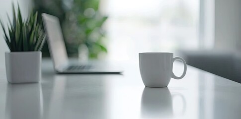 Wall Mural - Minimalist white office desk with laptop and coffee mug on a blurred background, with space for text, representing the concept of working from home