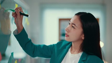 Aufkleber - Businesswoman writing with a green marker on a transparent glass board during a business meeting. The setting emphasizes collaboration and strategic planning in a professional environment