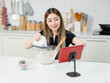 © Bangkok Click Studio - Young happy Asian beautiful woman wearing aprons smiling mixing dough for homemade baking cakes using electric mixer, looking tablet recipe guidebook in kitchen. Lifestyle at home learn online concept