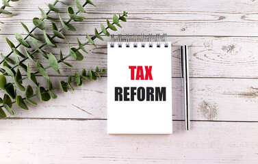 Poster - Notebook with the words Tax Reform in bold letters on a wooden desk, accompanied by a pen and green leaves