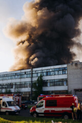 Wall Mural - Massive large blaze fire in the city with large column plume of smoke, blazing warehouse factory, storage building is burning, putting out the fire,  extinguish the fire, arson, burning house damage